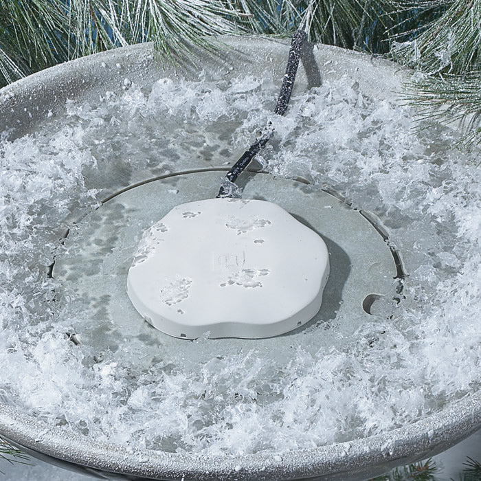 Heated Rock Bird Bath De-icer: White, round heater in a snow-filled bowl, maintains open water for birds in freezing temperatures.