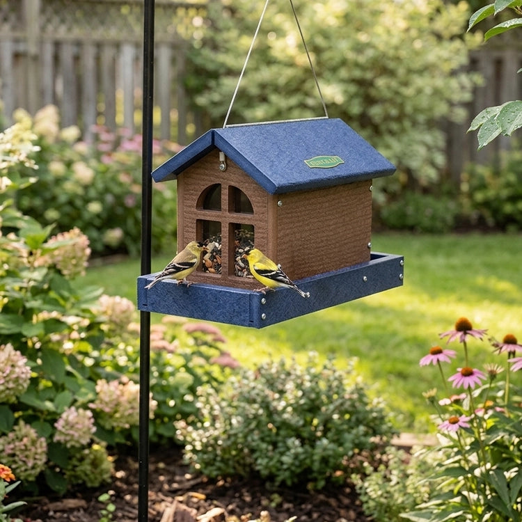 Barn bird feeder with seed and birds hanging form a pole in the backyard.