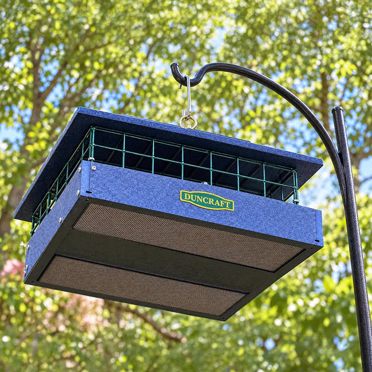 Hanging Duncraft bird feeder with a blue roof and green wire sides, set against a backdrop of green trees and blue sky.