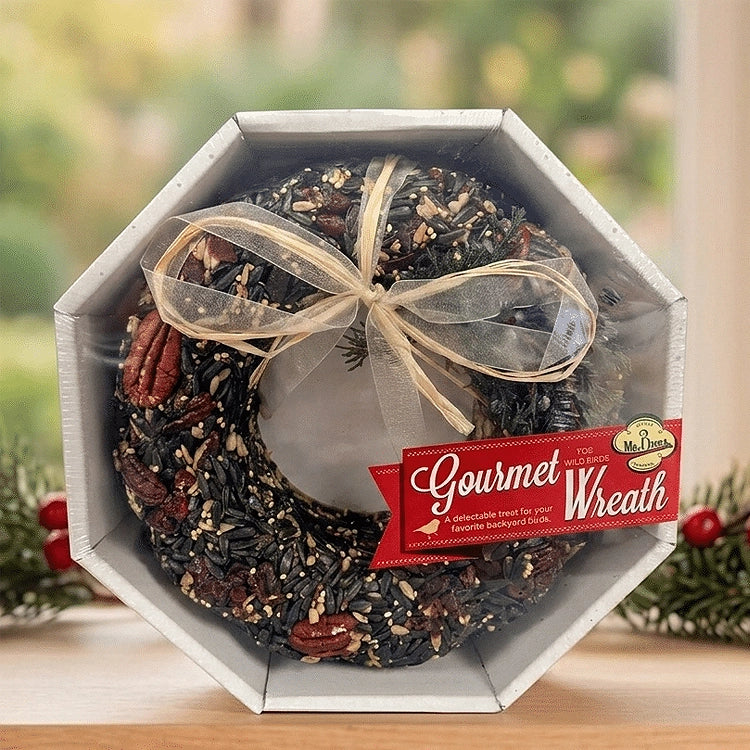 Mr. Bird Gourmet birdseed wreath with pecans and a gold bow in an octagonal gift box, displayed beside holiday greenery.