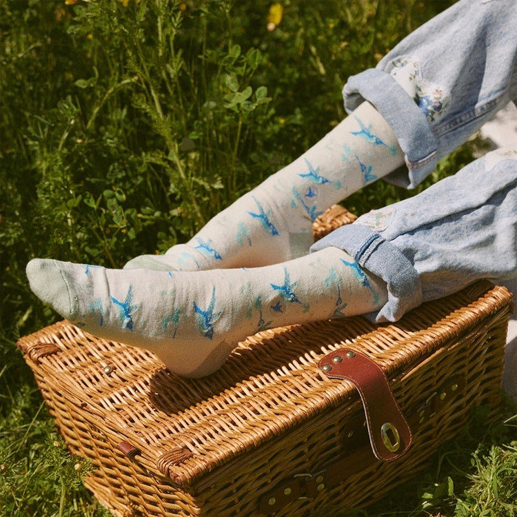 Close-up of cream and blue hummingbird socks worn with rolled jeans while relaxing outdoors on a picnic basket