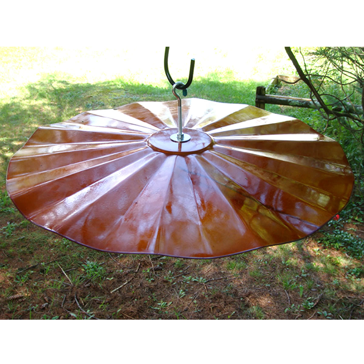 Extra Large Hanging Disk Squirrel Baffle, Copper Tint, shown outdoors; a circular, metal baffle designed to deter squirrels, hanging from a pole.