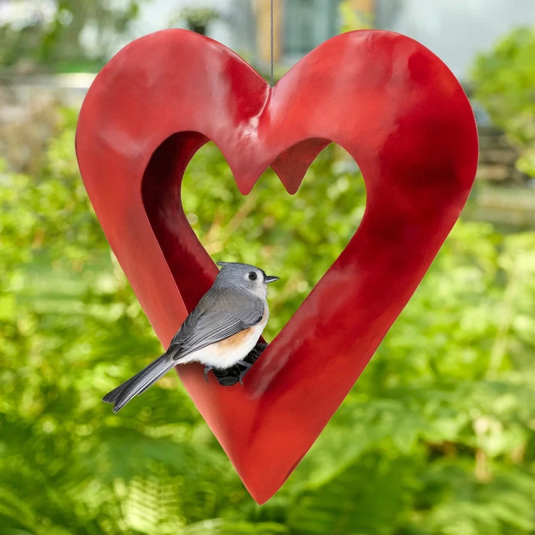 Fly Thru Red Heart Copper Bird Feeder with a grey songbird perched on it, showcasing its open-top heart shape and durable red copper finish.