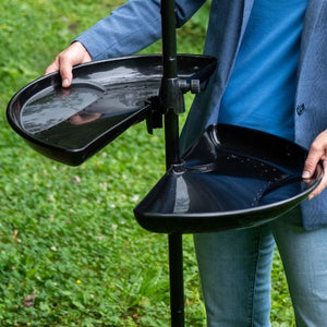 Person adjusting Brome Seed Buster Seed Tray and Catcher, featuring two adjustable black trays on a pole, designed to reduce bird seed waste and facilitate cleaning.