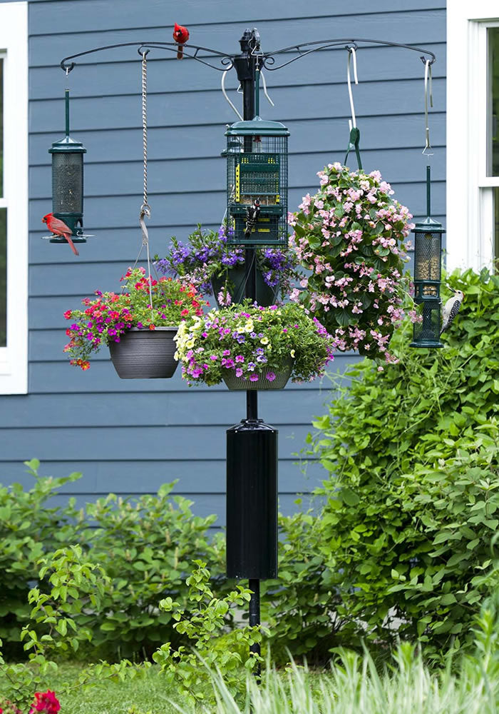 Brome Raccoon Buster® Guardian Pole System with bird feeder, flowers in baskets, and a bird perched on the feeder, ensuring raccoon and squirrel protection.