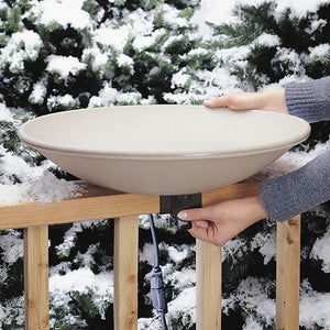 Person holding the All-Seasons Heated Deck Mount Bath on a snowy railing, showcasing its easy-clean tilt feature and thermostatically controlled heater for winter bird hydration.