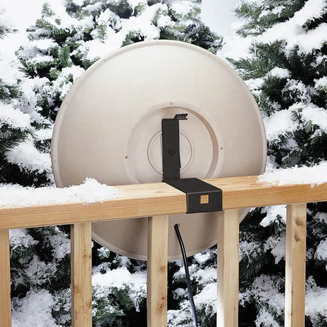 All-Seasons Heated Deck Mount Bath clamped on wooden railing, showcasing a circular design with visible flat-panel dish and cable, surrounded by snow-tipped trees.