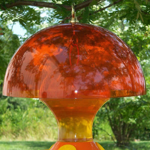 Orange Weather Baffle for oriole feeders with a dome shape, hanging from a tree, designed to keep nectar and jelly cool and fresh.