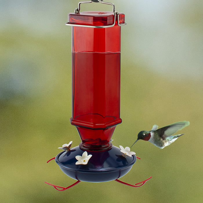 Patriotic Vintage Hummingbird Feeder with a red glass bottle, white flower-shaped feeding ports, blue base, and a hovering hummingbird nearby.