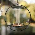 Contemporary Floating Sphere Hummingbird Feeder with glass reservoir, copper accents, and four flower feeding ports, designed for easy cleaning and filling. Holds 16 oz.