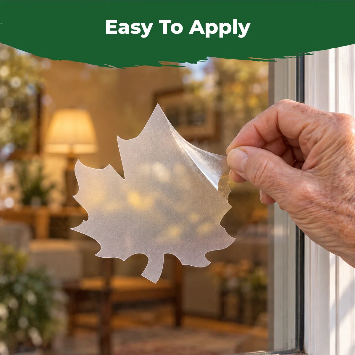 Close-up of a hand peeling and applying a translucent maple leaf bird-safe decal to a window.