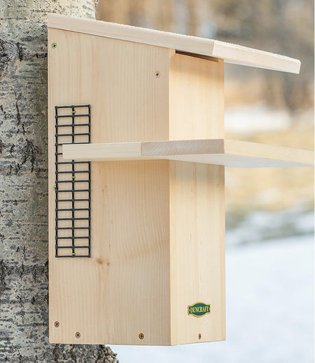 Duncraft Squirrel Den, a wooden birdhouse-style shelter on a tree with a sun porch, wire mesh ladder, and easy-clean front panel for baby squirrels.