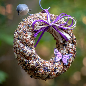 Wildfare Wreath: A bird perches on an edible wreath adorned with safflower, peanuts, tree nuts, and sunflower seeds, ready to hang in your bird-friendly yard.