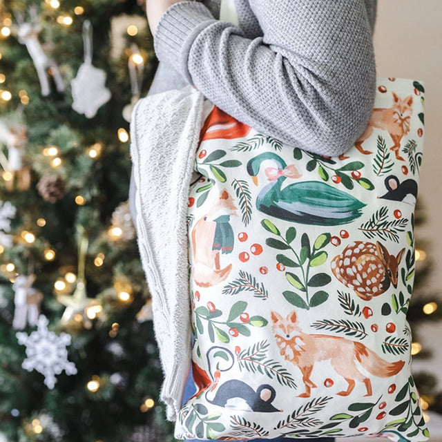 Person holding a Woodland Animals Tote with a nature-inspired pattern, standing near Christmas decorations.