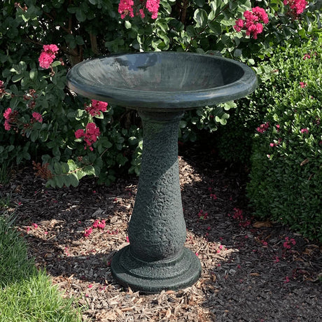 Birds & Beyond Fiber Clay Bird Bath, Hunter Green, featuring a stone pedestal with a full-sized basin, placed in a lush garden setting.