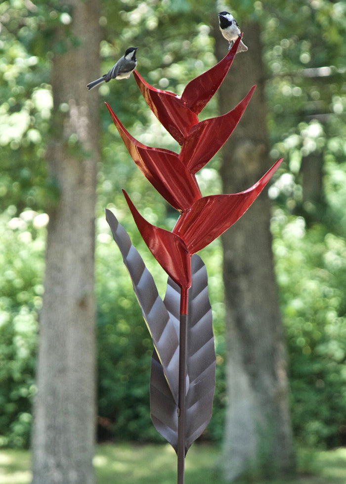 Heliconia Bird Feeder: A bird perches on a red, flower-shaped metal bird feeder designed for backyard use, featuring cascading seed and a durable, metallic finish.