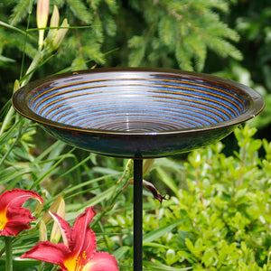 Circles Bird Bath Post, Cobalt Blue, in a garden setting with a black steel pole and concentric circles in the basin for bird perching.