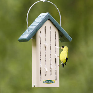 Duncraft Eco-Nester with a yellow bird perched on the feeder, pulling nesting material from slotted openings, featuring a wire hanger and squirrel-lock tabs.