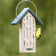 Duncraft Eco-Nester with a yellow bird perched on the feeder, pulling nesting material from slotted openings, featuring a wire hanger and squirrel-lock tabs.
