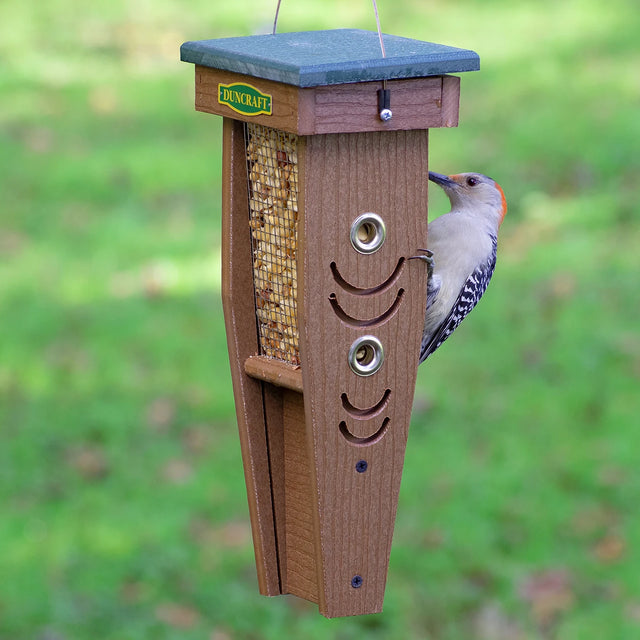 Duncraft Woodpecker Mesh Feeder with grooved perches, four feeding ports, and a top-lift roof for easy refilling, hanging outdoors with a bird feeding.