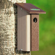 Downy Woodpecker Bird House mounted on a tree, featuring built-in predator guard and slim design, made from recycled materials.