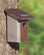 Duncraft Chickadee-Nuthatch Bird House mounted on a tree, featuring a 1-1/4 inch entry hole and a built-in predator guard for small birds.