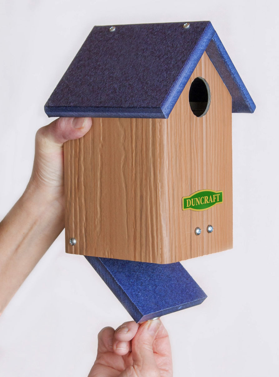 Hand holding Duncraft Bluebird Post-Tree Mount House, showcasing its sturdy design and ventilation slots for a cozy nesting area.