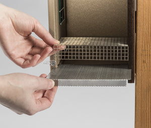 A person's hands holding a wire mesh grid for the Duncraft Bird-Safe® Premium Observation Bluebird House, featuring a built-in fledgling ladder.