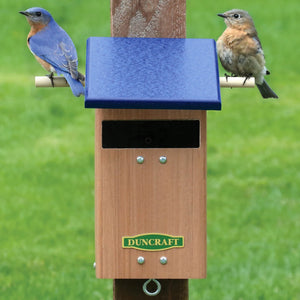 Duncraft Bluebird Watch Tower House with two perches, slotted entrance, and predator guard, mounted on a wooden post with bluebirds perched on it.