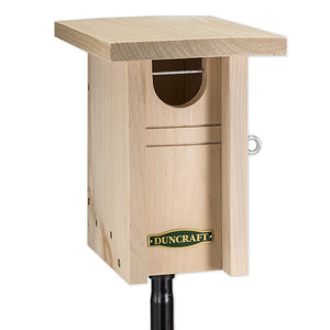 Duncraft Gilwood Bluebird Nest Box Bird House & Pole, featuring a wooden birdhouse with an oval entry hole, mounted on a black pole.