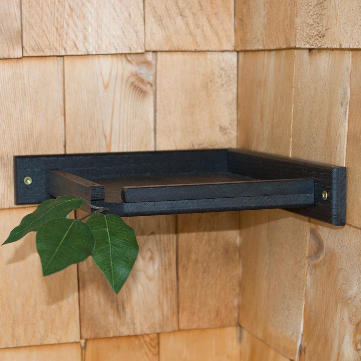 Under Deck Robins Nesting Platform on a black shelf with green leaves, designed for safe bird nesting, made from recycled plastic, includes mounting hardware.