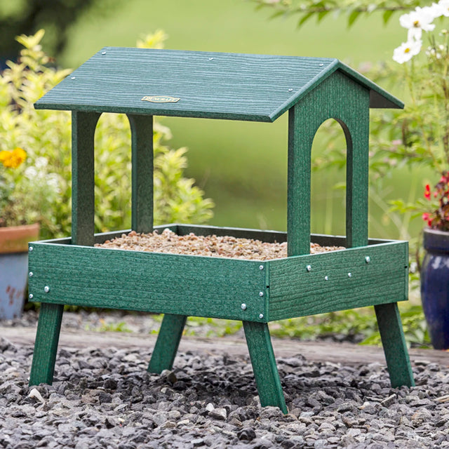 Duncraft Flight Deck Platform Feeder with Pole & Baffle, shown in a garden, features a sturdy roof, metal mesh flooring, and tall sectional pole for bird watching.