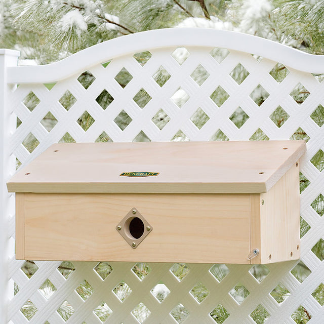 Duncraft Horizontal Winter Roost mounted on a white fence, featuring a 1-1/2 inch entry hole, two long perches, and a front latch for easy cleanout.