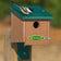 Duncraft Chickadee Roosting House with Swivel Mounting Bracket features a perched black-capped chickadee, showcasing its small entry hole and sturdy post mount.