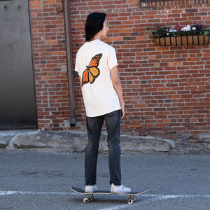 Monarch Metamorphosis T-Shirt: Person skateboarding in a white shirt featuring a butterfly design on the back, symbolizing the Monarch butterfly's transformation.