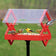 Duncraft Double Diamond Post Platform Feeder with clear roof, hosting goldfinches and chickadee, features multiple entry points and a durable red frame.