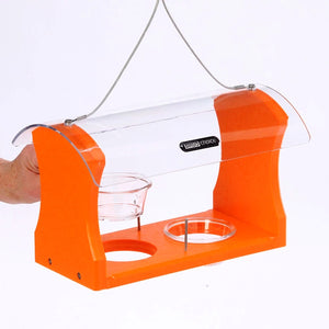 Hand holding the Fruit & Jelly Oriole Feeder, featuring two plastic dishes and metal pegs for fruit, with a clear-plastic roof and durable steel hanging cable.