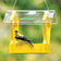 Duncraft Heritage Platform Feeder, Yellow, with a clear roof, features an American Goldfinch on the mesh tray, offering easy access and seed protection.