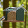 Bird feeder with bird seeds and a bird perched on it against a blurred natural background