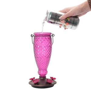 Hand pouring Perky-Pet® Ready-To-Use Clear Hummingbird Nectar, 16 oz., from an aluminum can into a pink glass.