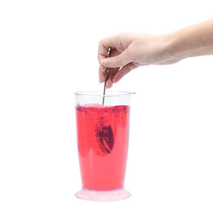 Perky-Pet® Red Hummingbird Nectar Concentrate, 12 oz., shown being mixed with water in a glass by a hand holding a spoon.