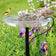 Stonecreek Waterfall Rock Pump on a bird-bath with bubbling water, attracting a goldfinch and dove, set in a lush garden.