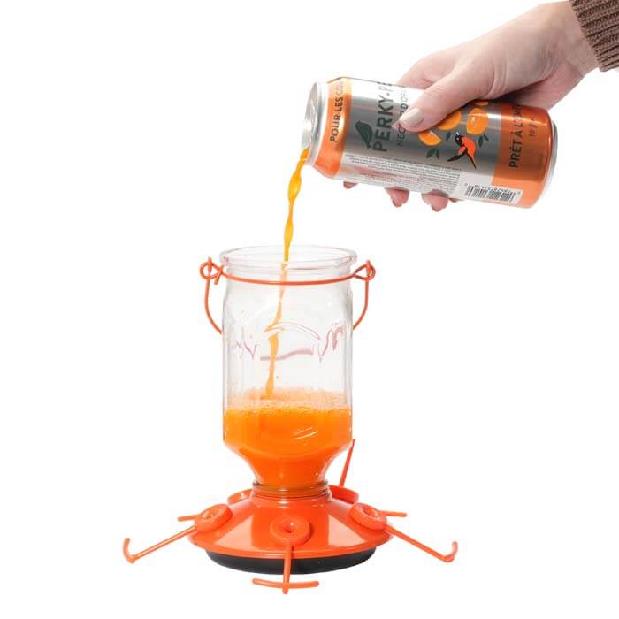 Hand pouring Perky-Pet® Ready-To-Use Orange Oriole Nectar, 16 oz., from a can into a glass jar, highlighting ease of use and oriole-friendly recipe.