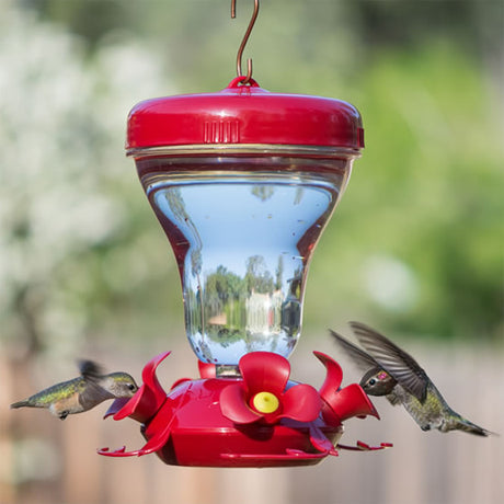 Magnolia Hummingbird Feeder with four feeding ports, red flower perches, and a clear reservoir. Hummingbirds flying around it, showcasing its attractive design and functionality.