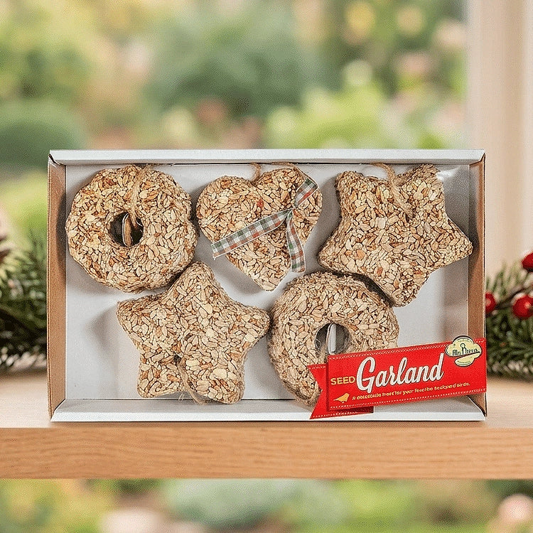 Mr. Bird Seed Garland gift box displayed on a wooden shelf beside holiday greenery.