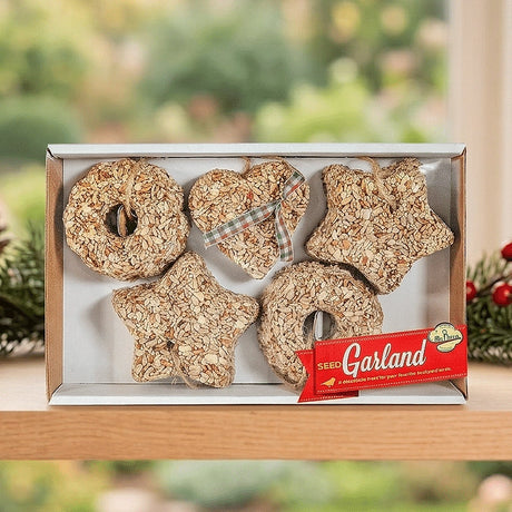 Mr. Bird Seed Garland gift box displayed on a wooden shelf beside holiday greenery.