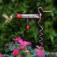 Flower Pot Hummingbird Feeder with a clear glass tube and red bead, attached to a copper wire stand, attracting a hummingbird feeding.