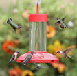 JB's Hummingbird Feeder with four feeding ports, red tray, and clear glass reservoir, surrounded by hummingbirds in flight and feeding.