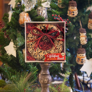 WildFeast Bird Seed Wreath displayed by a Christmas tree, featuring a solid seed, nut, and fruit mix, ready to hang with a raffia bow, perfect for bird feeding.