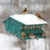 Squirrel Resistant Birder's Choice: Green bird feeder with snow, five finches feeding, metal rods, squirrel-proof design, and adjustable perch for selective bird attraction.